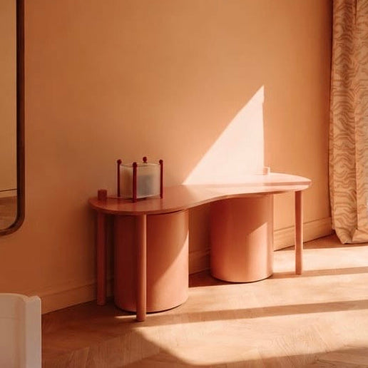 Minimalist pink console table against a beige wall with a large mirror and curtain.